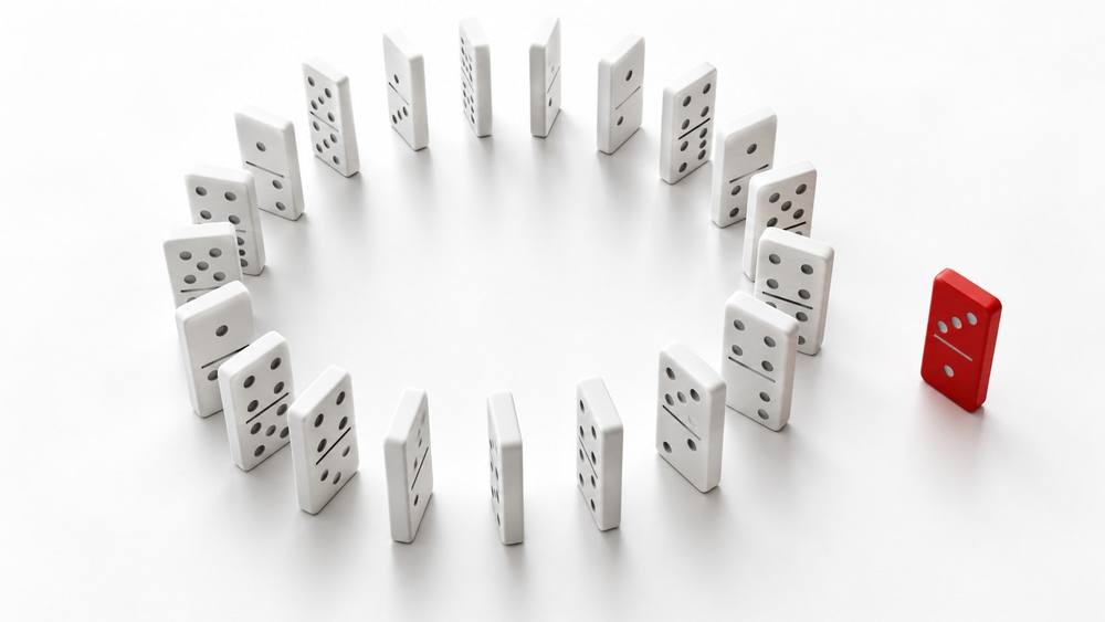 Ring of white dominoes with one red domino standing apart on a white surface